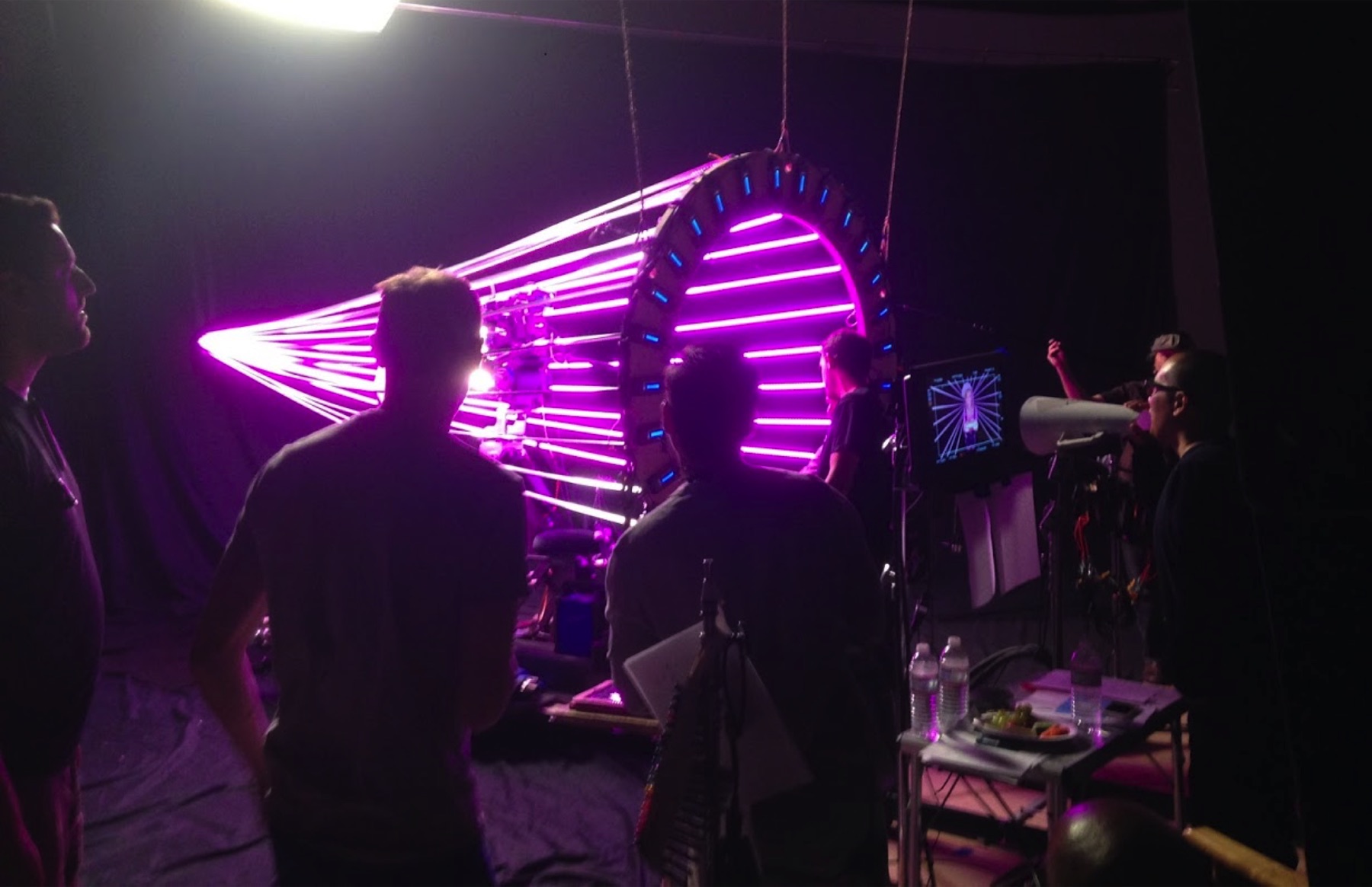 A Pilot Content crew on a dark set, watching a large ring of purple and blue lights.